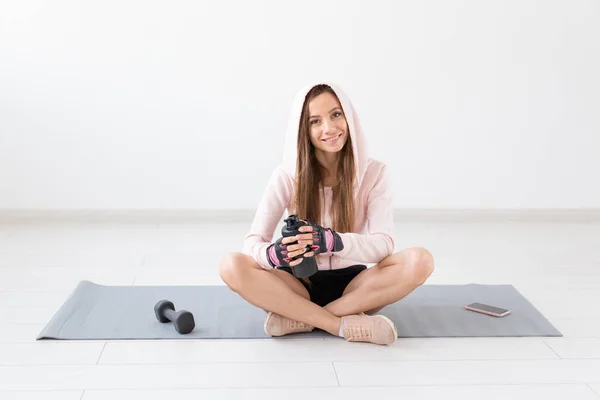 Mode de vie sain, personnes et concept sportif - Femme souriante assise sur un tapis de yoga et de l'eau potable après un entraînement dur — Photo