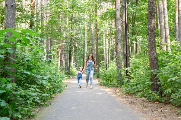 Familie-, vrijetijds- en natuur concept - portret van een moeder met haar dochtertje wandelen in het groene park in de zomer — Stockfoto