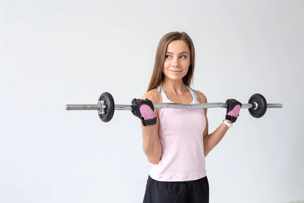 Sport, fitness e concetto di persone - Adatta agli esercizi di una giovane donna con una barra del peso, facendo i suoi bicipiti — Foto Stock