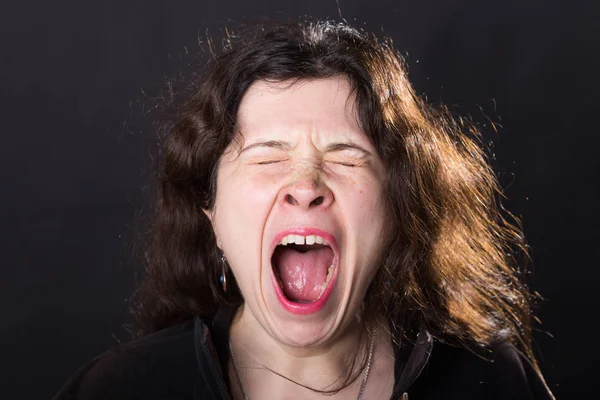 Negative emotions concept - Scared screaming young woman standing over black background.