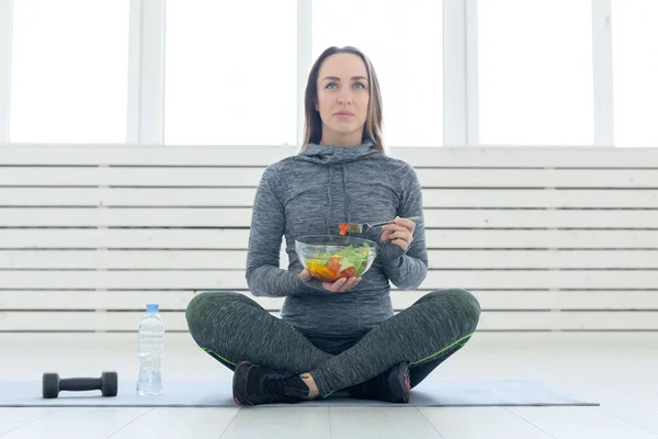 Deporte, estilo de vida saludable y concepto de personas: mujer joven con ensalada y una mancuerna sentada en el suelo — Foto de Stock