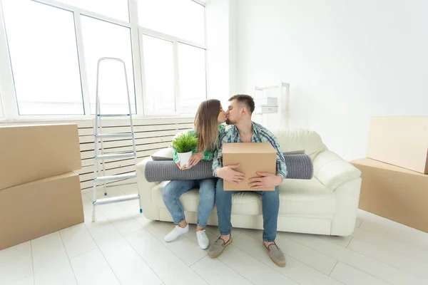 Charmigt ungt par i casual kläder hålla saker i händer och sitter på soffan kyssar att gratulera varandra med inflyttnings — Stockfoto
