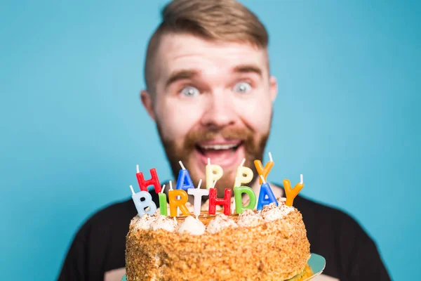 青い背景に立って彼の手に幸せな誕生日ケーキを保持クレイジー面白い肯定的な男ヒップスター。ジョークと休日の挨拶の概念. — ストック写真