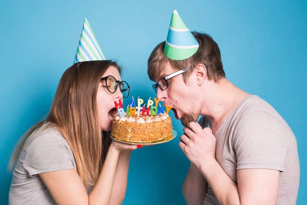 Bizarre Młoda para dziewczyna i chłopiec w kapelusze papieru chcą ugryźć kawałek tort gratulacyjny. Koncepcja urodzin i gratulacji. — Zdjęcie stockowe
