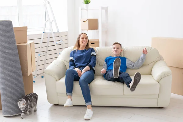 Feliz bela mãe jovem e um filho positivo estão sentados no sofá ao lado de seu gato curvo escocês e estão felizes em se mudar para um novo apartamento . — Fotografia de Stock