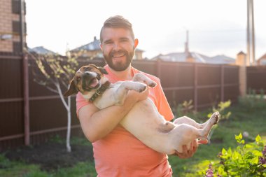 Sakallı pozitif genç adam sevgili köpeği Jack Russell Terrier tutuyor ve güneşli bir yaz gününde onun kır evinin bahçesinde ortak bir dinlenme tadını çıkarıyor. Onların dört için aşk kavramı