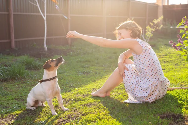 Femme gaie positive jouant avec son chien bien-aimé Jack Russell Terrier dans la cour de sa maison de campagne par une journée d'été ensoleillée. Concept d'amour pour les animaux et les loisirs familiaux . — Photo
