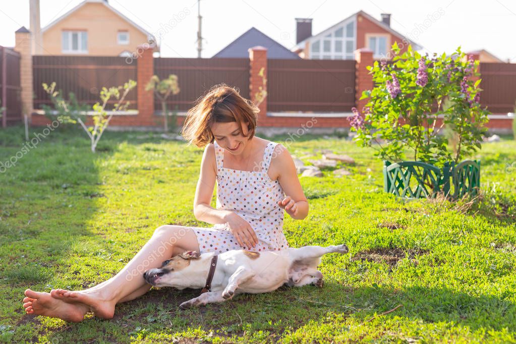 Young woman with her jack russell terrier dog playing on the grass outside