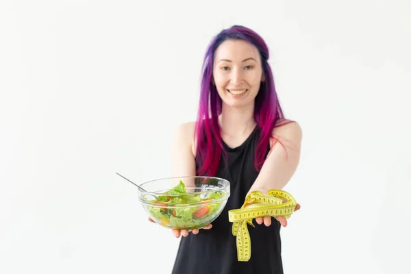 Young blurred asian girl hipster colored hair holding in hands a measuring tape and vegetable salad posing on a white background. Healthy eating concept. Advertising space. — 스톡 사진