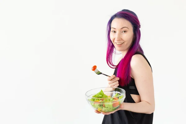 Позитивна змішана дівчина-гіпстер з кольоровим волоссям, що їсть легкий грецький салат після фізичних тренувань на білому тлі з копіювальним простором. Концепція правильного харчування та схуднення . — стокове фото