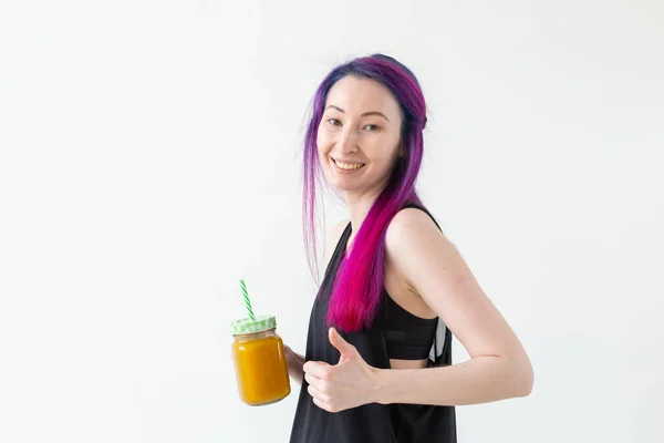 Retrato de uma jovem mista positiva e menina hipster com cabelo colorido bebendo smoothie proteína de frutas e mostrando os polegares para cima em um fundo branco com espaço de cópia. Conceito de estilo de vida saudável — Fotografia de Stock