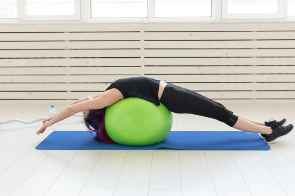 Joven chica delgada hace ejercicio y estiramiento para la espalda en un fitball verde En el gimnasio brillante. Concepto de espalda y ligamento saludable . — Foto de Stock