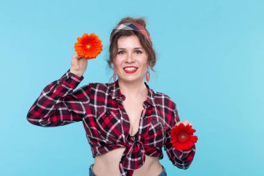 Elinde mavi bir arka plan üzerinde poz iki kırmızı ve turuncu çiçek tutan Büyüleyici genç gülümseyen kadın. Güzellik ve öz bakım kavramı.
