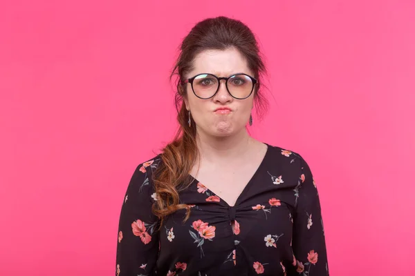 Retrato de una joven enojada descontenta con gafas en una chaqueta negra posando sobre un fondo rosa brillante. Concepto de descontento y desacuerdo . — Foto de Stock