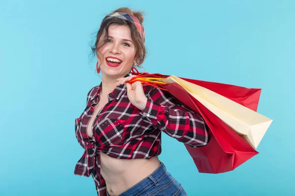 Glückliche junge schöne Frau in kariertem Hemd und Jeans und mit einer Tasche vor blauem Hintergrund. Konzept des Einkaufs und des Einkaufs neuer Produkte. — Stockfoto