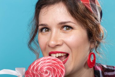 Mavi arka plan üzerinde lolipop yiyen güzel genç kadının portresini kapatın