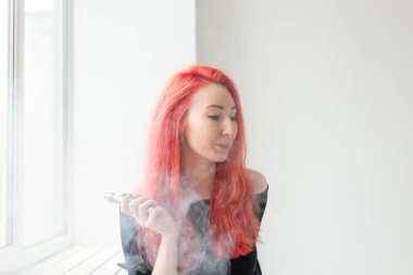 Gençlik ve bağımlılık kavramı - genç kızıl saçlı kadın pencere yakınında vape sigara