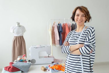 Onun aksesuarları ve dikiş makinesi ile masaüstünün arka planda duran olumlu bir genç kadın terzi kesici Portresi. Benzersiz tasarım ürünleri oluşturma kavramı.
