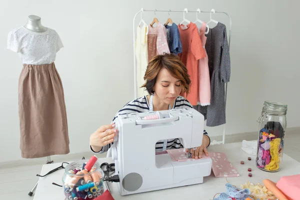 Joven mujer talentosa ropa de diseñador cose su nuevo producto sentado en su escritorio con la máquina de coser y accesorios. Concepto de pasatiempos y profesiones . — Foto de Stock