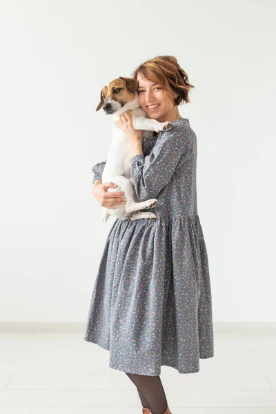 매력적인 미소 젊은 여자는 그녀의 마음에 드는 개 잭 러셀 테리어를 들고 세련된 회색 드레스에. 컨셉 좋아하는 개. — 스톡 사진