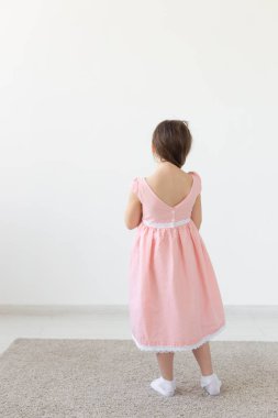 Beyaz bir arka plan üzerinde bir tasarımcı elbise poz pembe bir elbise içinde büyüleyici bir küçük kız prenses arka görünümü. Çocuk kıyafetleri kavramı. Kopyalama alanı