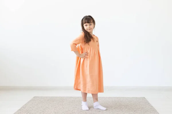 Pretty dziecko dziewczyna pozowanie do aparatu, w pomarańczowej krótkiej sukni, białe tło z kopią przestrzeni — Zdjęcie stockowe