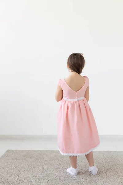 Bakifrån av en charmig liten flicka prinsessa i en rosa klänning poserar i en designerklänning på en vit bakgrund. Begreppet barnkläder. Kopiera utrymme — Stockfoto