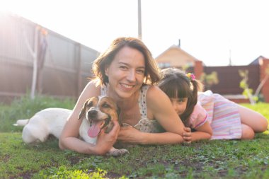 Olumlu Genç Anne ve kızı ve köpek kendi kır evinin çim üzerinde yatıyor ve sıcak havalarda hafta sonu boyunca ortak bir dinlenme zevk