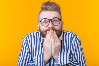 Gözlüklü şaşıran genç erkek hipster ağzını kapatır ve sarı bir arka plan üzerinde poz güler. Çizim ve sürpriz kavramı.