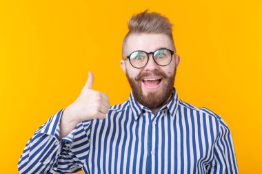Bir işaret arama gösteren sarı bir arka plan üzerinde poz bıyık lı ve sakallı neşeli yakışıklı genç hipster adam. Telefon ve iletişim konsepti.