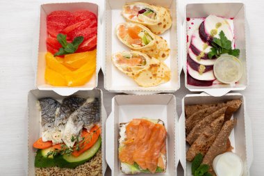 Öğle yemeği kutularında gün için sağlıklı yemekler seti beyaz bir masa üzerinde duruyor. Doğru beslenme menüsü kavramı proteinler, yağlar ve karbonhidratdengesi