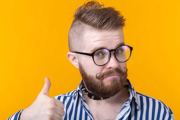 Retrato de cerca de un joven hipster guapo mostrando pulgares hacia arriba posando sobre fondo amarillo. El concepto de buena suerte y éxito . — Foto de Stock