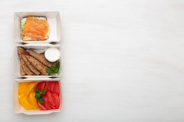 Τρεις τύποι σάντουιτς με σνακ και τηγανίτες και πορτοκάλια με γκρέιπφρουτ είναι σε ένα κουτί γεύματος σε λευκό τραπέζι. Έννοια της υγιεινής διατροφής. Διαφημιστικός χώρος. — Φωτογραφία Αρχείου