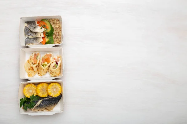 Three kinds of lunch boxes with fish and vegetables lie on a white table. Space for advertising. Healthy eating concept