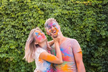 Tatil, bayram ve insanlar kavramı - mutlu çift yüzlerinde çok renkli toz ile eğleniyor