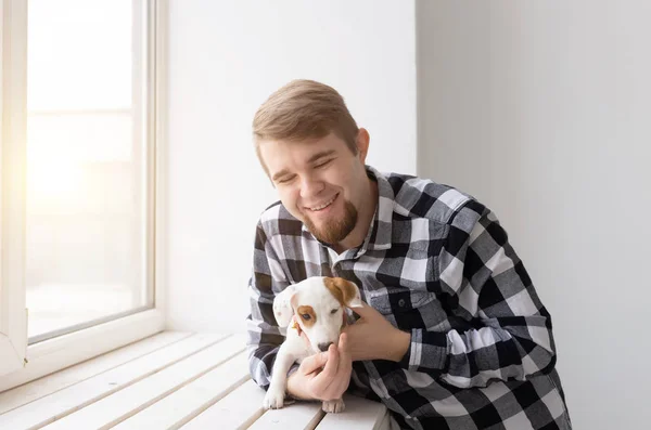 People and pet concept - Happy man holding a dog Jack Russell Terrier over window background — Stock Photo, Image