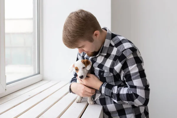 people, pets and animals concept - young man hugging puppy near window on white background