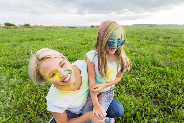 Felicidad, festival Holi y el concepto de vacaciones - Madre y su hija cubierta de polvo de color sonriendo sobre el fondo de la naturaleza —  Fotos de Stock