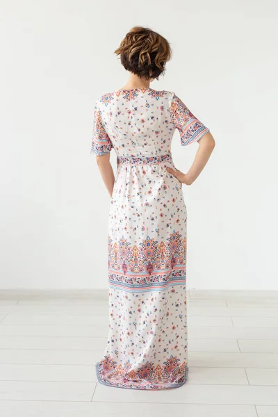 Hátulnézet egy fiatal karcsú nő egy hosszú mintás ruhát állt szemben egy fehér falat. Az egyedi termékek koncepciója — Stock Fotó