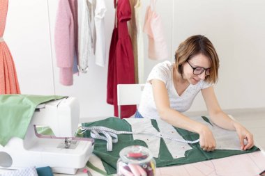 Üniversitede bir giysi tasarımcısı genç güzel kız öğrenci çalışma ve bir dikiş makinesi ile bir masada oturan ilk tezyapar. Giyim tasarım konsepti.