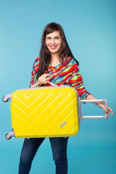 Portrait d'une belle jeune femme brune avec une valise jaune dans les mains posant sur un fond bleu. Concept de voyage et de tourisme . — Photo