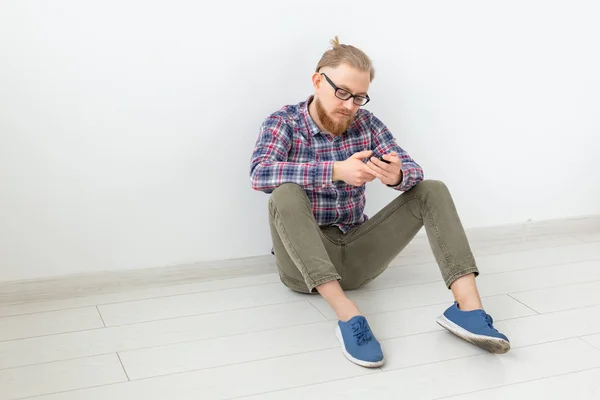 Hombre barbudo sentado en el suelo con teléfono, fondo claro con espacio para copiar — Foto de Stock