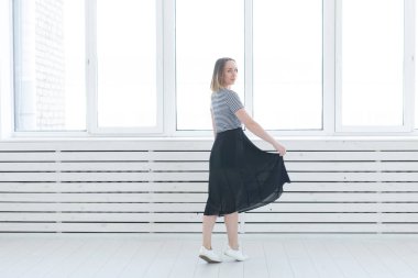 Gençlik, stil ve insan kavramı - siyah etek ve spor ayakkabı pencerenin yanında duran genç kadın