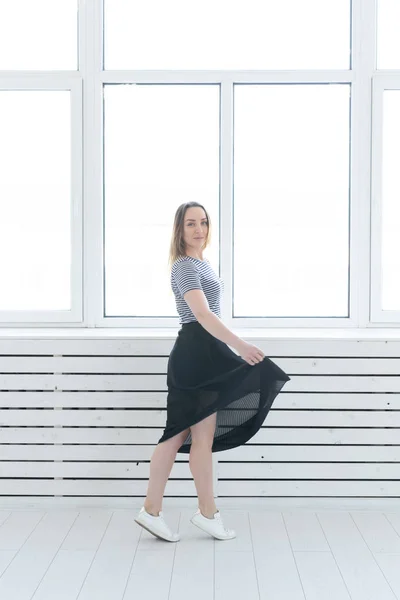 Youth, style and people concept - young woman on black skirt and sneakers standing near the window