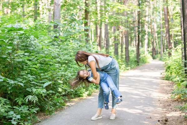 Rodina a příroda koncept - atraktivní mladá žena bavit se svou malou dcerou v parku — Stock fotografie
