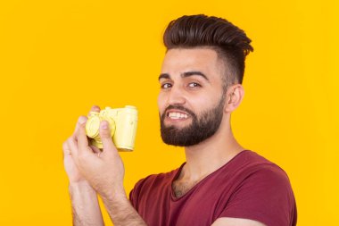 Elinde sarı bir Vintage kamera tutan bir sakal ile pozitif yakışıklı genç bir adamın portresi. Fotoğrafçılık konsepti.