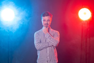 Carming genç gülümseyen hipster adam kırmızı ve mavi stüdyo aydınlatma arka plan karşı poz olduğunu. Dalgın adam kavramı.