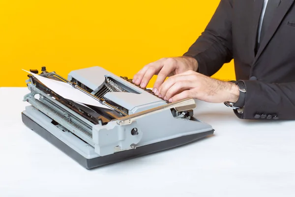 Tett på forretningsmann eller leder i formell dress som skriver tekst på en skrivemaskin med gul bakgrunn. Konseptet forretnings- og kontorarbeid – stockfoto