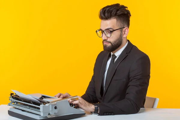 Joven hombre de negocios guapo en ropa formal escribiendo texto en una máquina de escribir posando sobre un fondo amarillo. Lugar para la publicidad. Concepto empresarial . — Foto de Stock