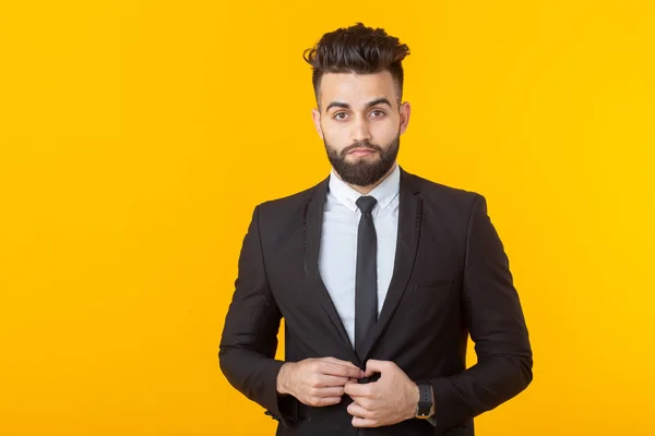 Charming young self-confident businessman wearing formal clothes posing on a yellow background. Concept of business and success.